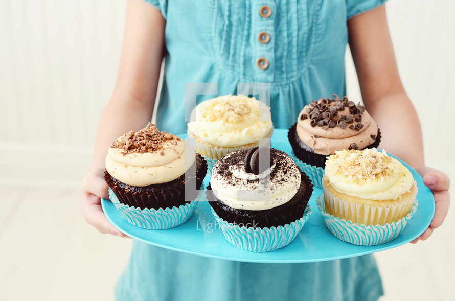 a girl child holding a plate of cupcakes 