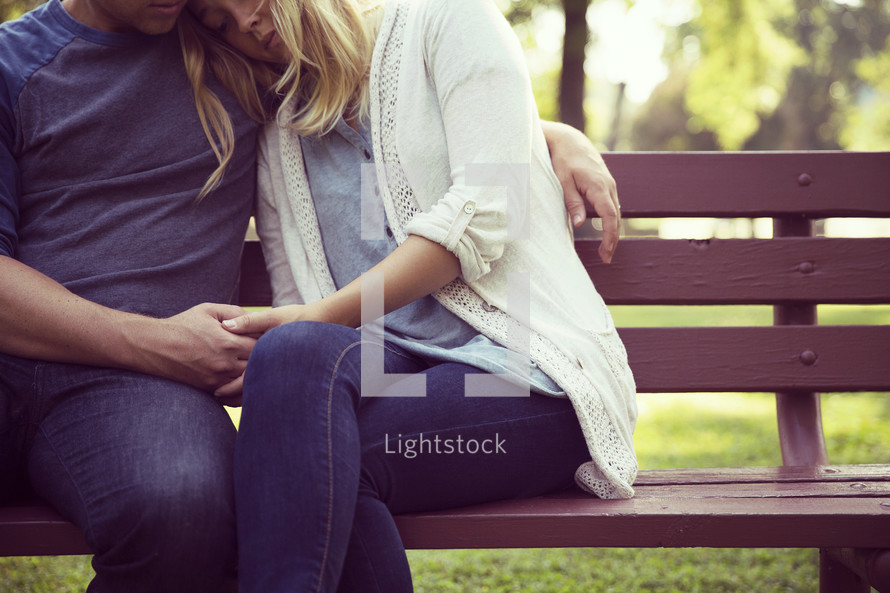 a couple snuggling on a park bench 