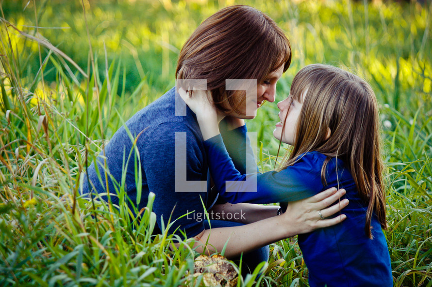 Mother and daughter embracing while sitting in tall grass.