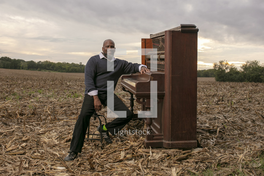 a man playing a piano in a plowed field 