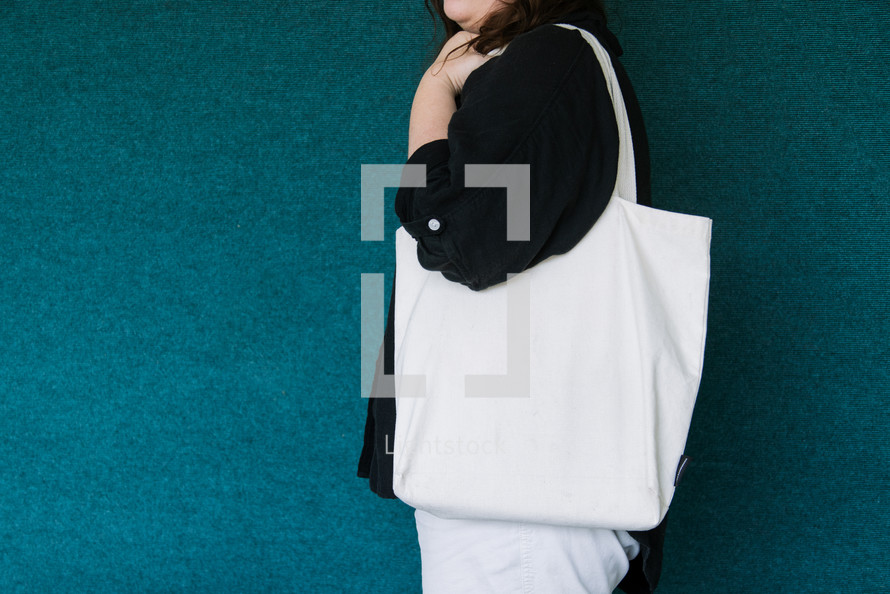 Woman in a black shirt holding a blank canvas tote bag on her shoulder.