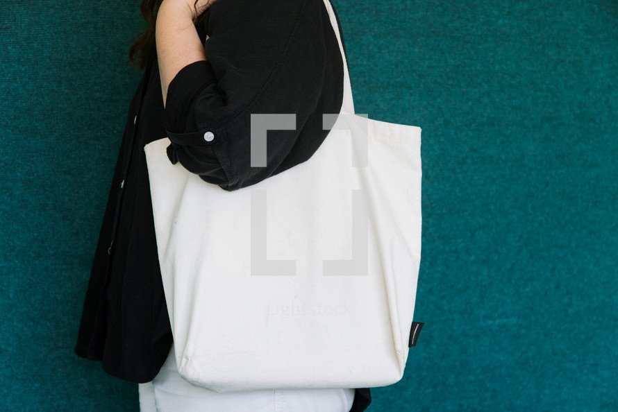 Woman in a black shirt holding a blank canvas tote bag on her shoulder.