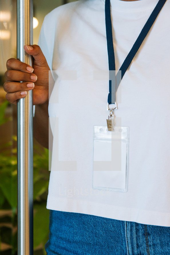 Woman in a white tshirt wearing a large lanyard while holding a door open.