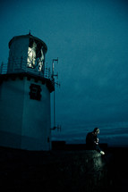 man sitting beneath a lighthouse at night 