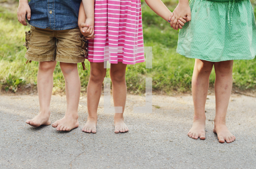 Three barefooted children holding hands.