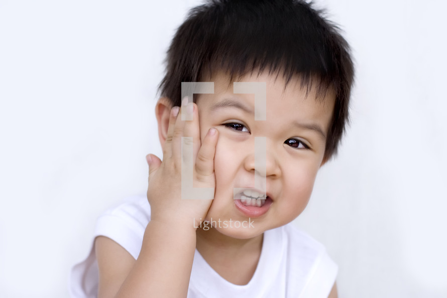 a toddler boy with his hand on his face 