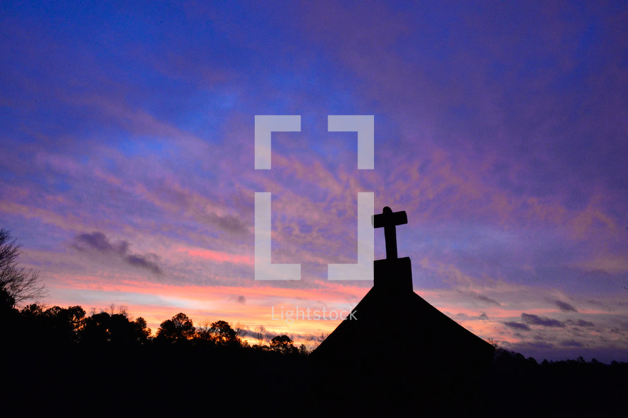 silhouette of a cross on a roof at dusk 