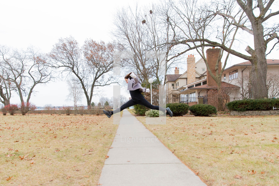 a girl leaping over a sidewalk 