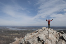 man standing at the top of a mountain with his hands raised in worship to God