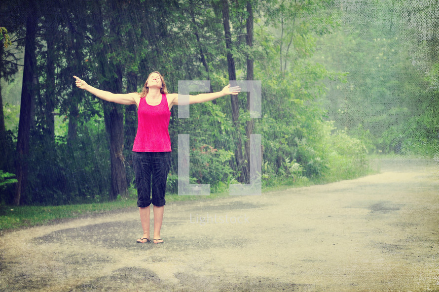 Woman walking outside in the rain with arms wide open.