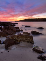 sunrise over rocks along a beach shore