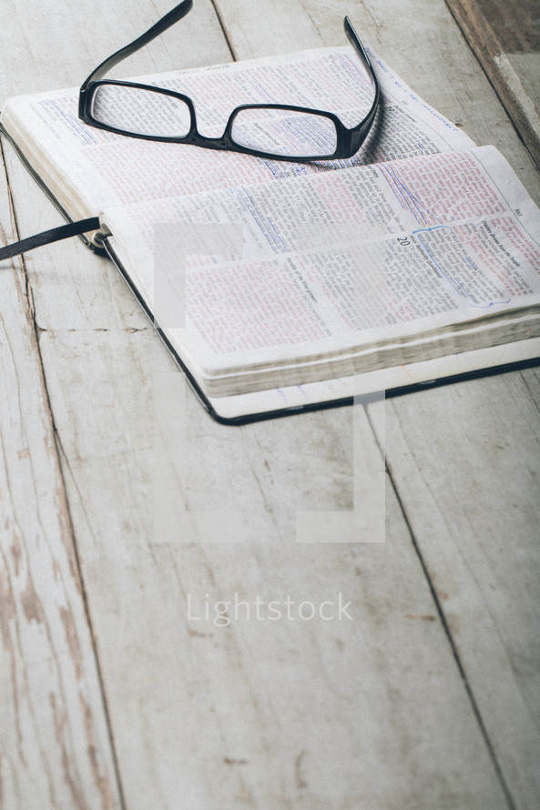 Reading glasses on pages of open Bible laying on wooden table.