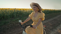 Rural woman in timeless dress riding retro styled white bicycle on country road alone near sunflowers field. Vintage fashion, amazing adventure, countryside activity, healthy lifestyle.