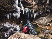 A man sitting next to a frozen waterfall. 