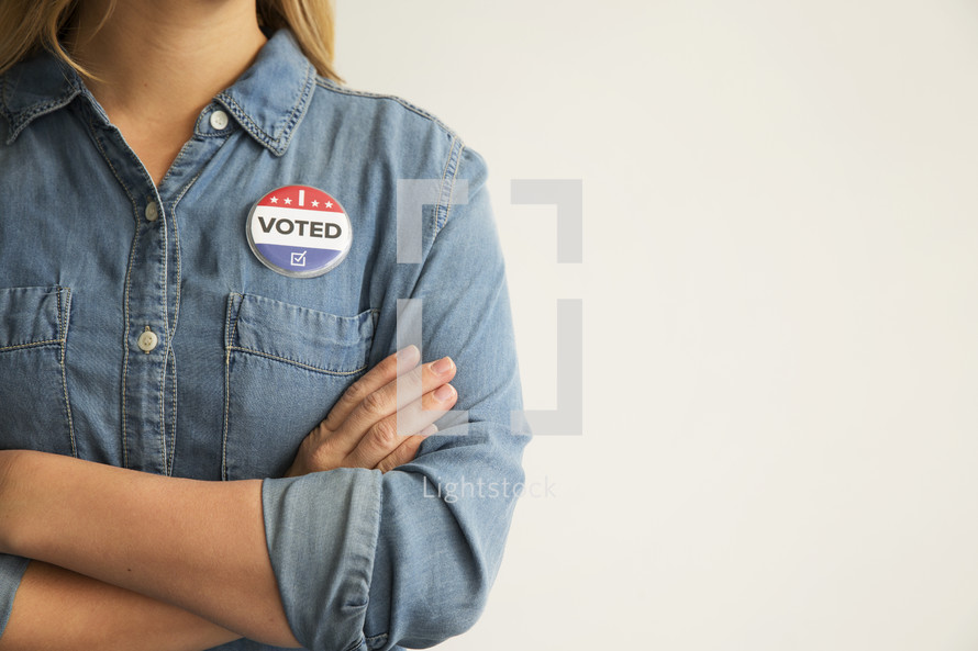 A woman with arms crossed wearing a "I Voted," button.
