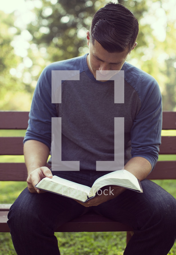 a man sitting on a park bench reading a Bible 