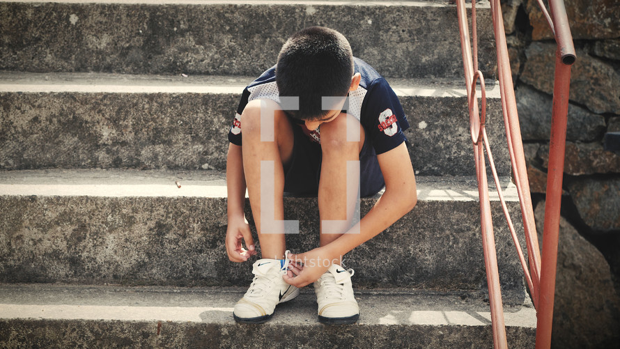 young man sitting on steps tying his shoes 