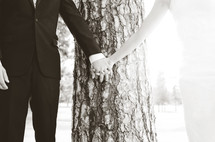 A man and woman holding hands in front of a tree.