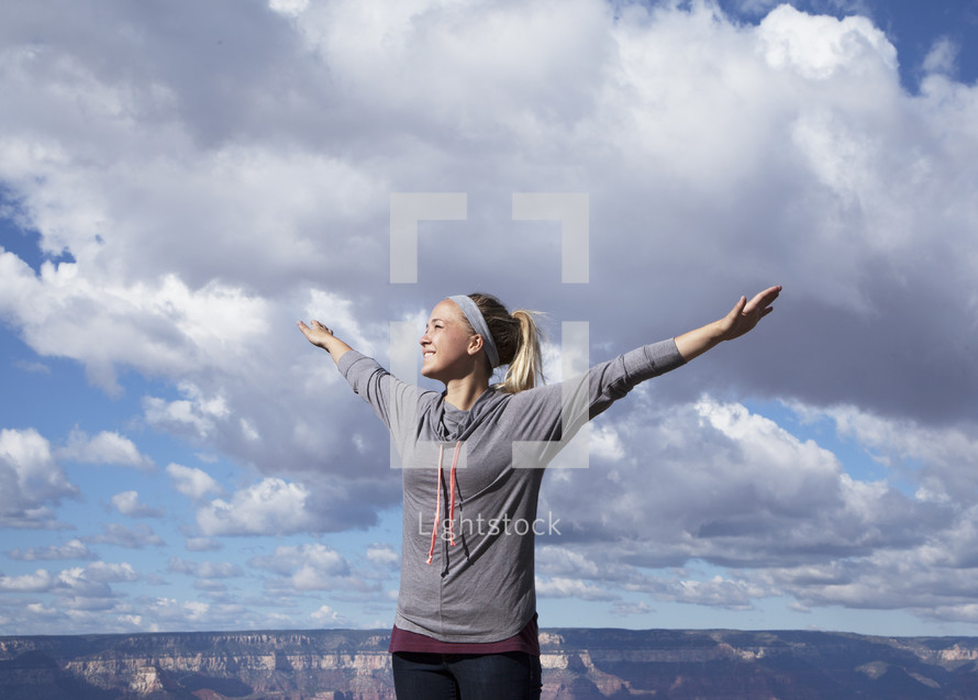 a woman standing at the top of a canyon with open arms 