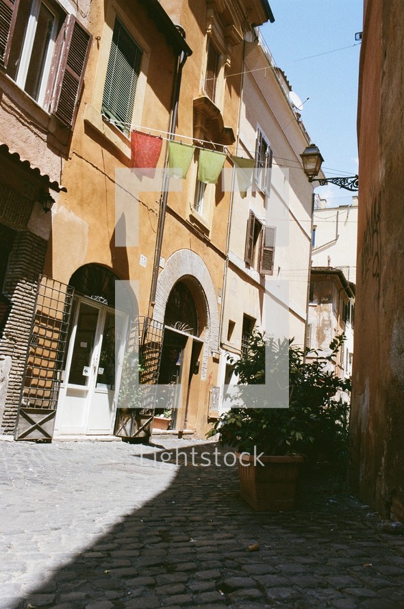 clothes hanging on a clothesline between buildings over a cobblestone street 