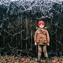A boy child standing in front of a fence covered in frost 