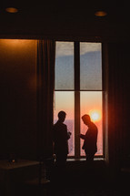 men standing by a window at sunset looking at their cellphones 