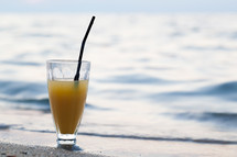 Glass of cocktail on beach near water