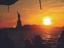 tourists looking out at the statue of liberty at sunset 