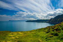 A dramatic sky over bright green field of grass and sea cliffs in Northern Ireland.