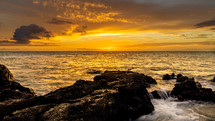 Golden sunset over the ocean as seen from a rocky beach 