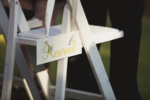 A reserved sign hanging on a white folding chair