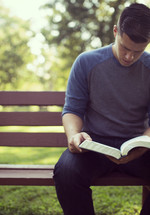 a man sitting on a park bench reading a Bible 