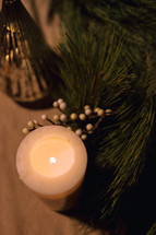 White candle next to a pine garland.