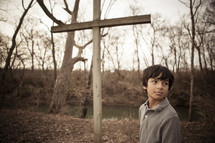 teen boy standing in front of a wood cross outdoors 