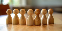 Group of wooden people standing in a row on a wooden table.