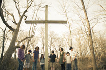 holding hands in prayer around a cross 