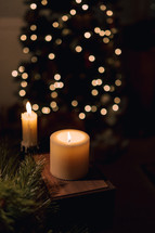 Lit candles with a Christmas tree in the background.
