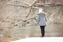 a woman in a coat looking at a river 