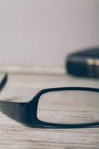 single lens of a pair of reading glasses and a Bible