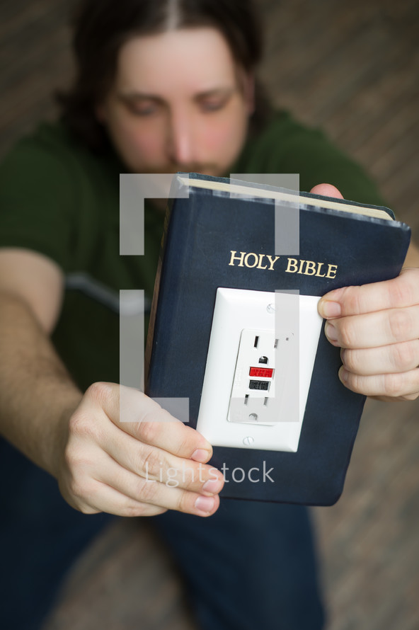 power of scripture - man holding a Bible with an outlet and power cord plugged in - get plugged in