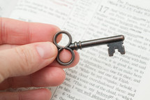 hand holding a key over the pages of a Bible