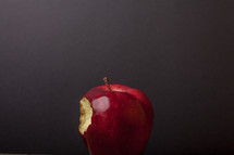 A red apple with a bite out of it, on a black background.