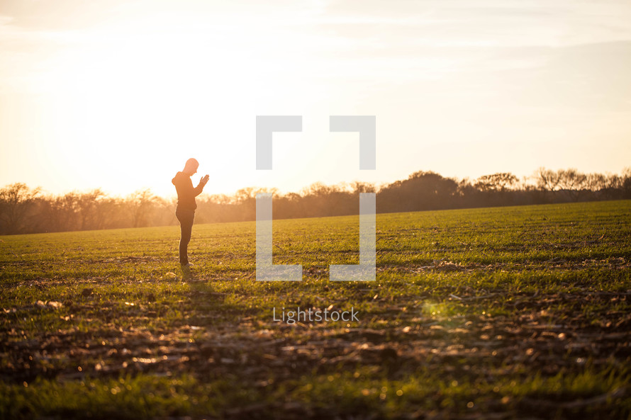 silhouette of a man praying in a field glowing under sunlight