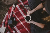 a person sitting on a blanket drinking coffee 