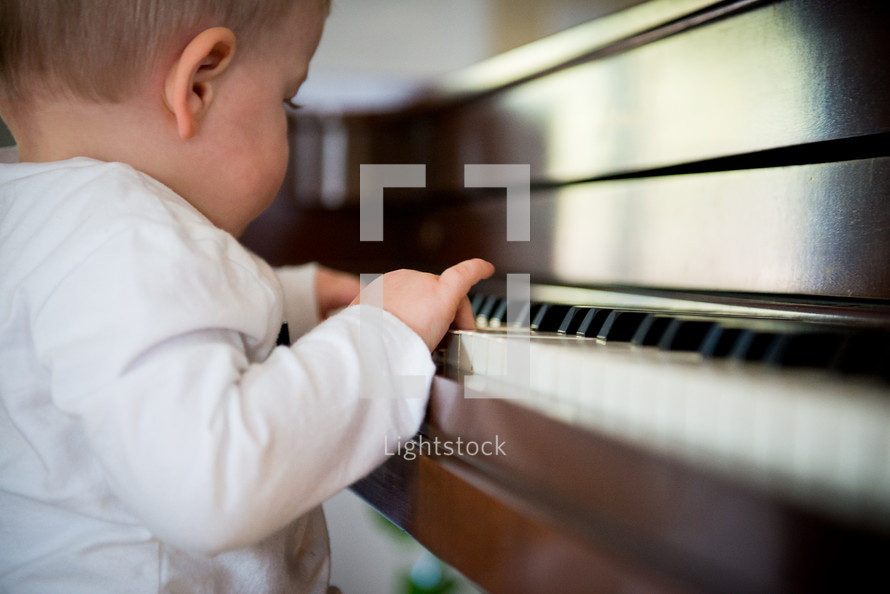toddler with his hands on a piano 