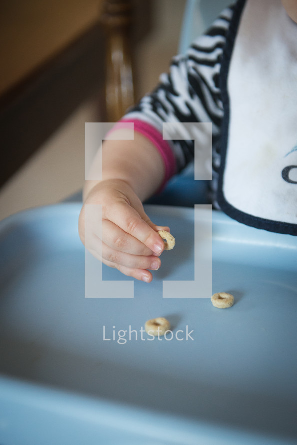 an infant in a highchair eating Cheerios 