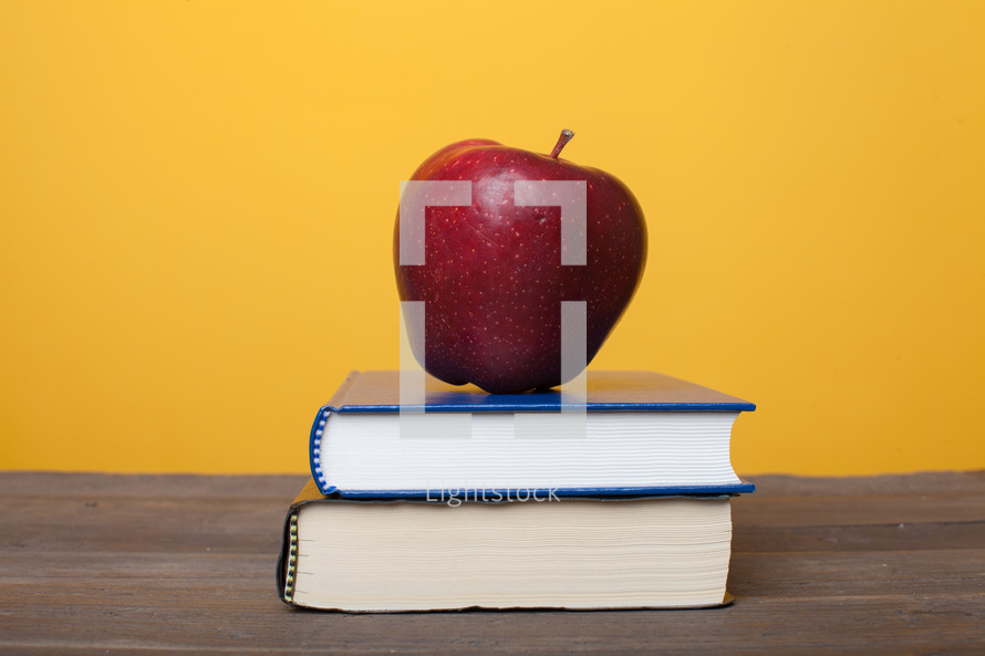 apple on a stack of books on a teacher's desk 