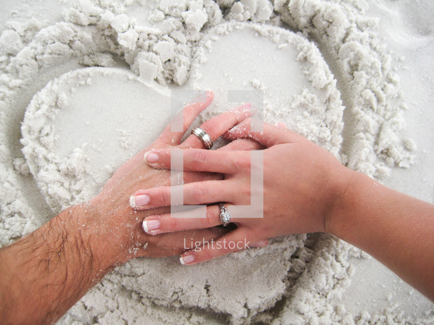 hands of a married couple on a heart drawn in the sand 