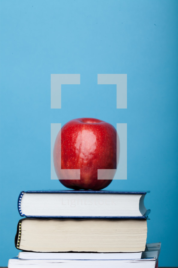 A red apple atop a stack of books with a blue background.