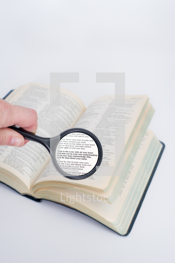 Hand holding a magnifying glass on a Bible open to the Book of Proverbs.